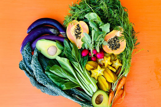 A bountiful, colorful selection of local produce arranged in the shape of a heart against an orange background