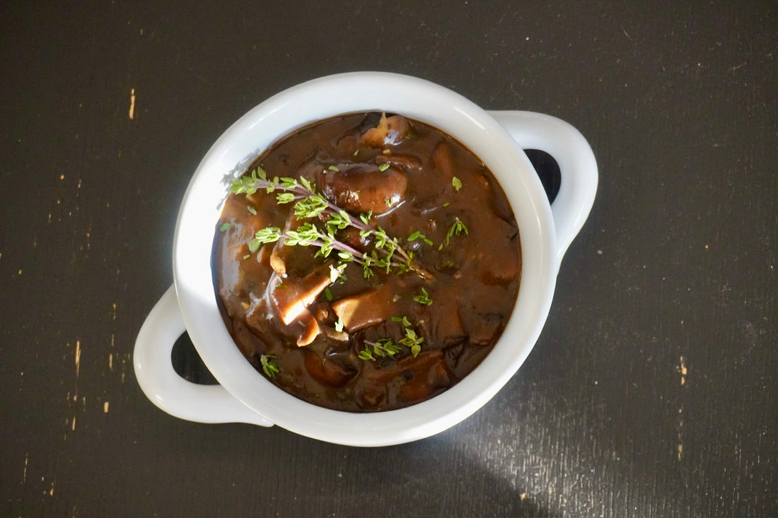 Rich mushroom gravy served in a ceramic bowl with a side of fresh herbs for garnish.