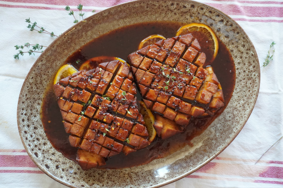 A golden-brown glazed tofu roast scored in a diamond pattern and served on a bed of fresh orange slices.